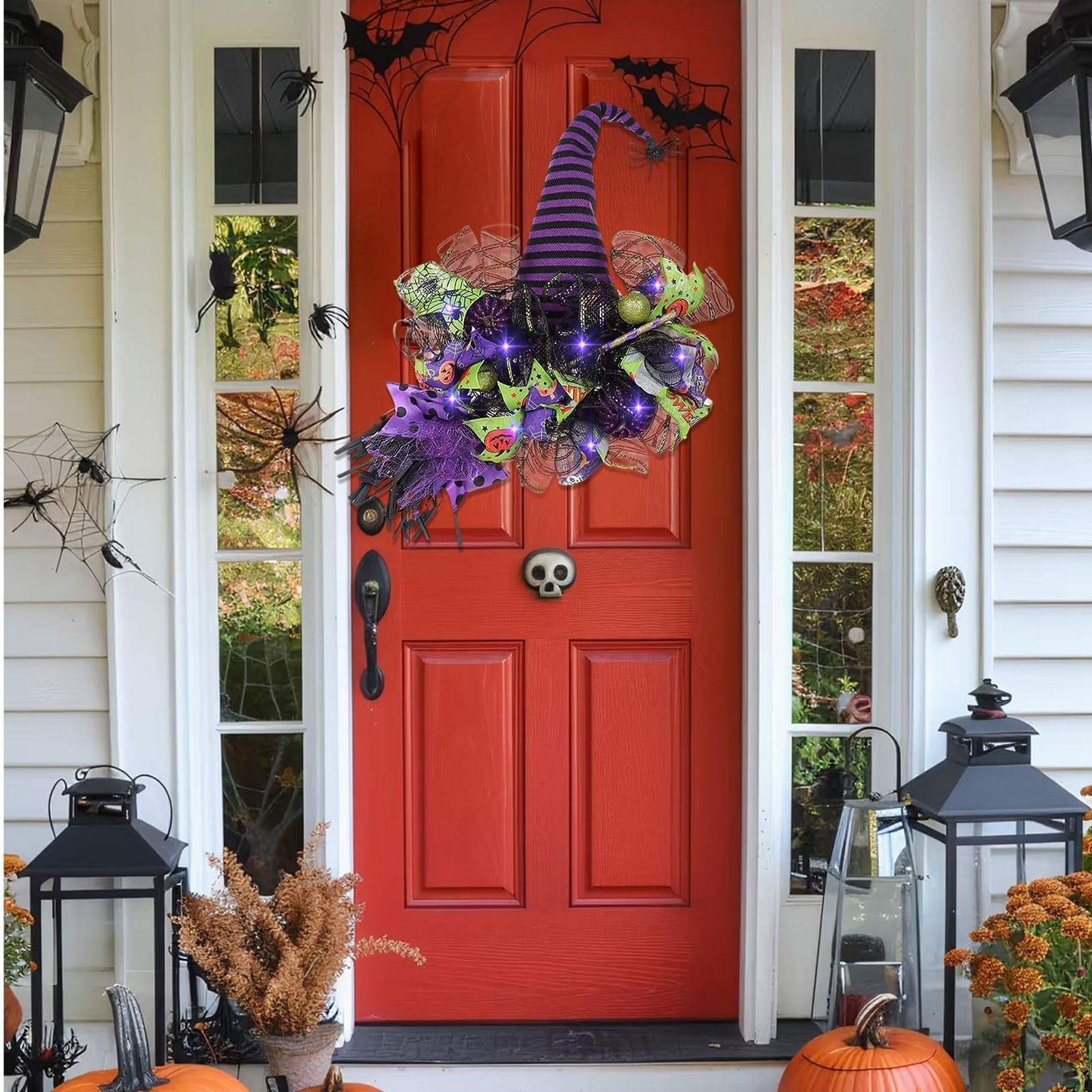Halloween witch hat wreath with purple lights and mesh decor hanging on a red front door with spider web decorations.
