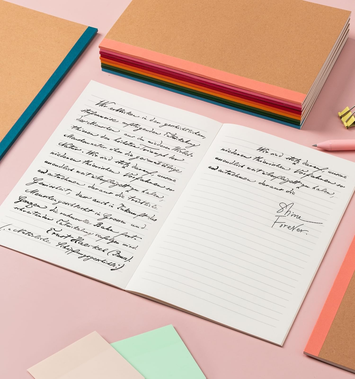 Open notebook with handwritten text and a stack of colorful A5 notebooks in the background.