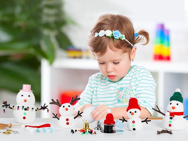 Young girl crafting air dry clay snowmen with various accessories on a table