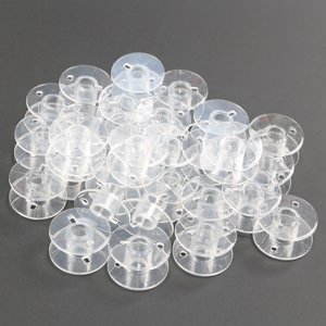 Pile of 30 transparent plastic sewing machine bobbins on a gray surface
