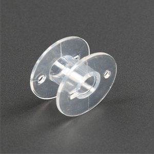Single transparent plastic sewing machine bobbin shown at an angle on a dark gray surface.