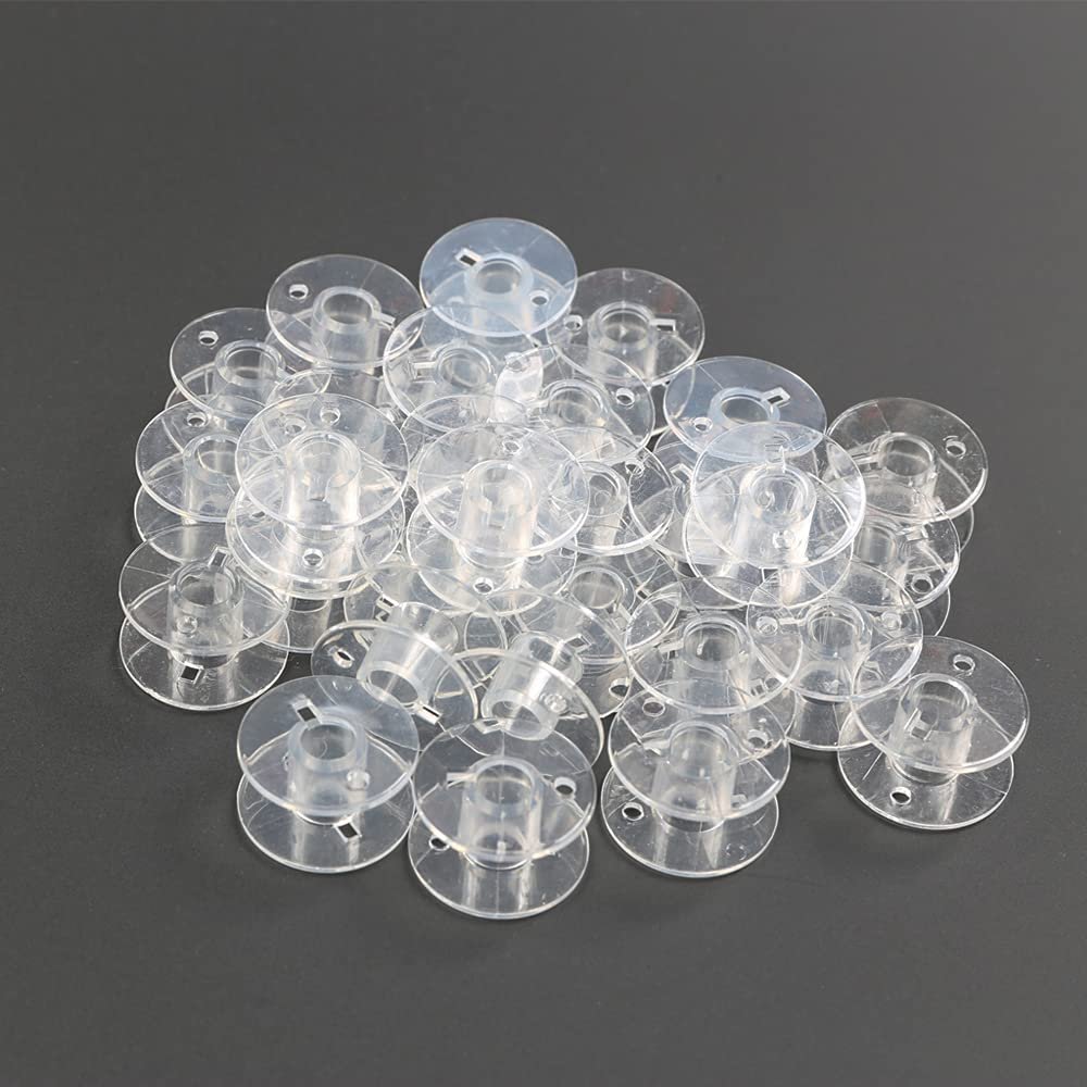Pile of 30 transparent plastic sewing machine bobbins on a dark gray surface.