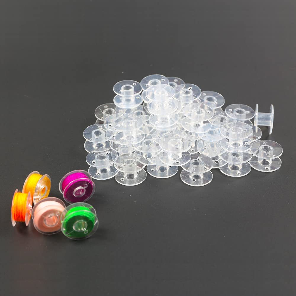 Pile of transparent plastic sewing machine bobbins with four colorful spools of thread on the side.