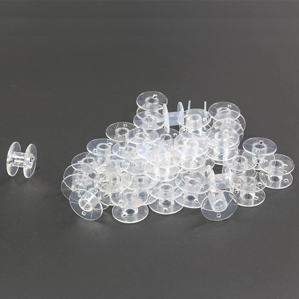 Pile of transparent plastic sewing machine bobbins on a dark gray surface, with one bobbin to the left.