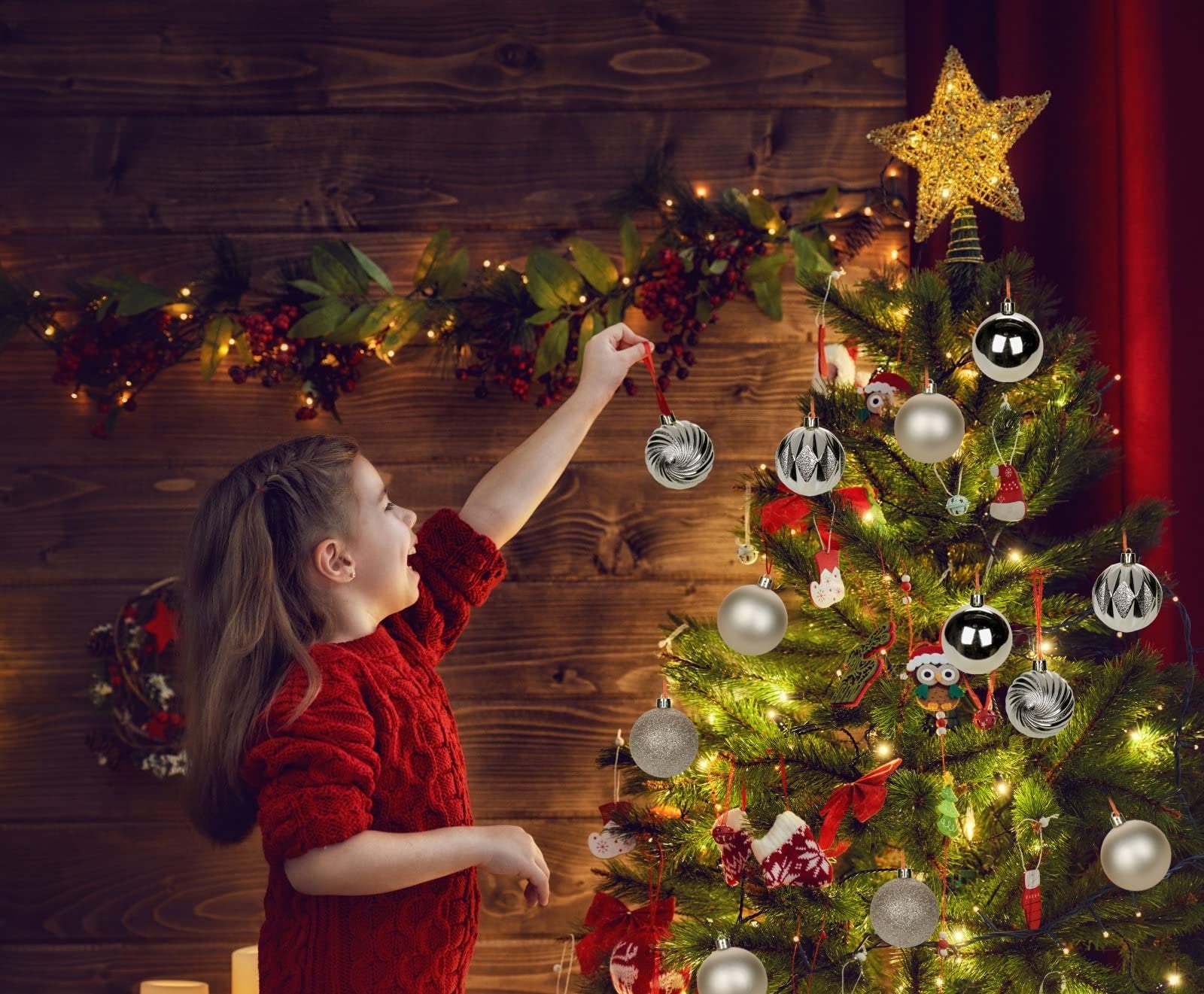 Young girl in red sweater decorating a Christmas tree with silver ornaments and lights.