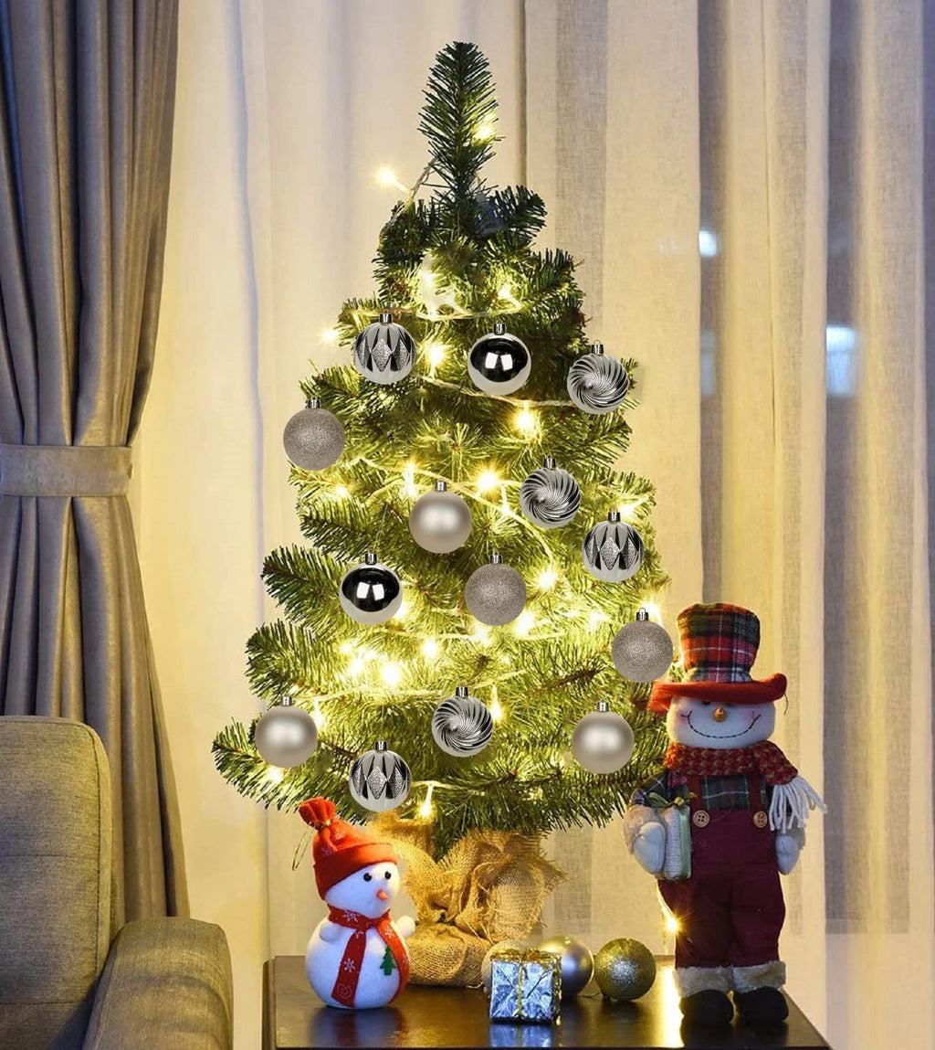 Decorated Christmas tree with champagne shatterproof ornaments and festive figures on a table.