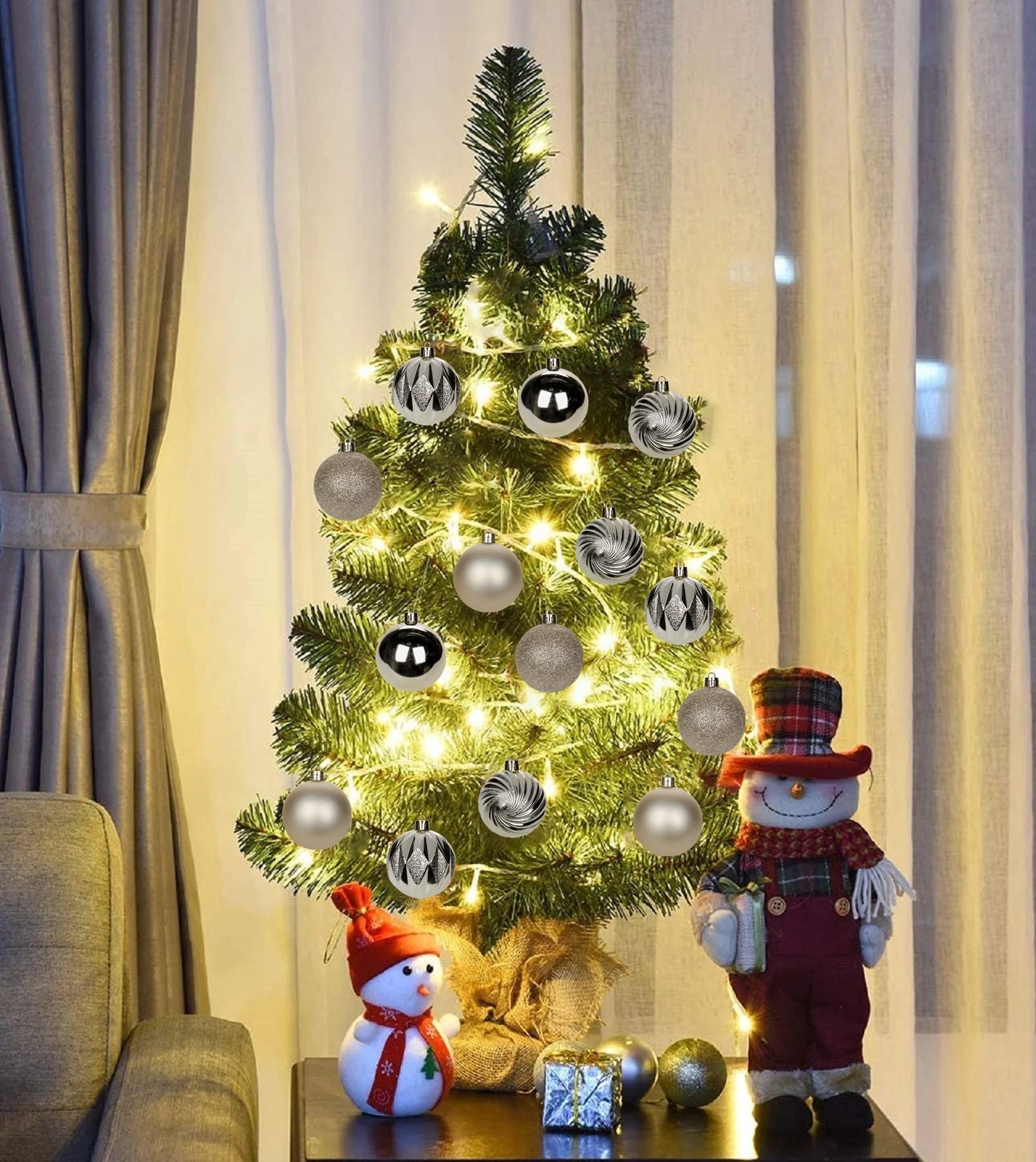 Decorated Christmas tree with champagne shatterproof ornaments and festive figures on a table.