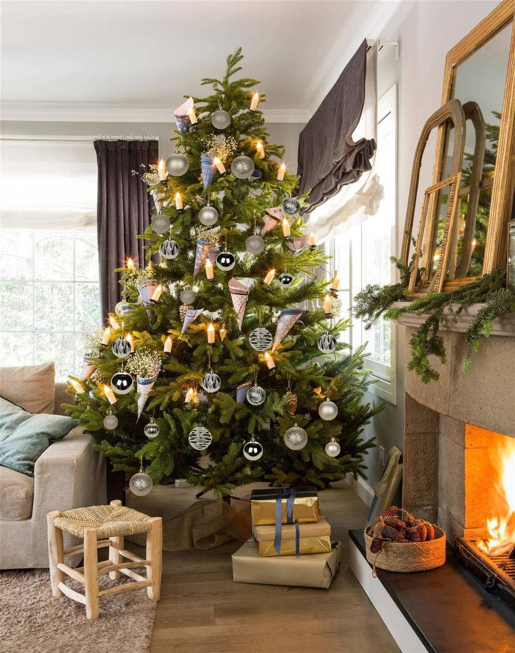 Decorated Christmas tree with champagne shatterproof ornaments and lights, near a fireplace with a fire burning.
