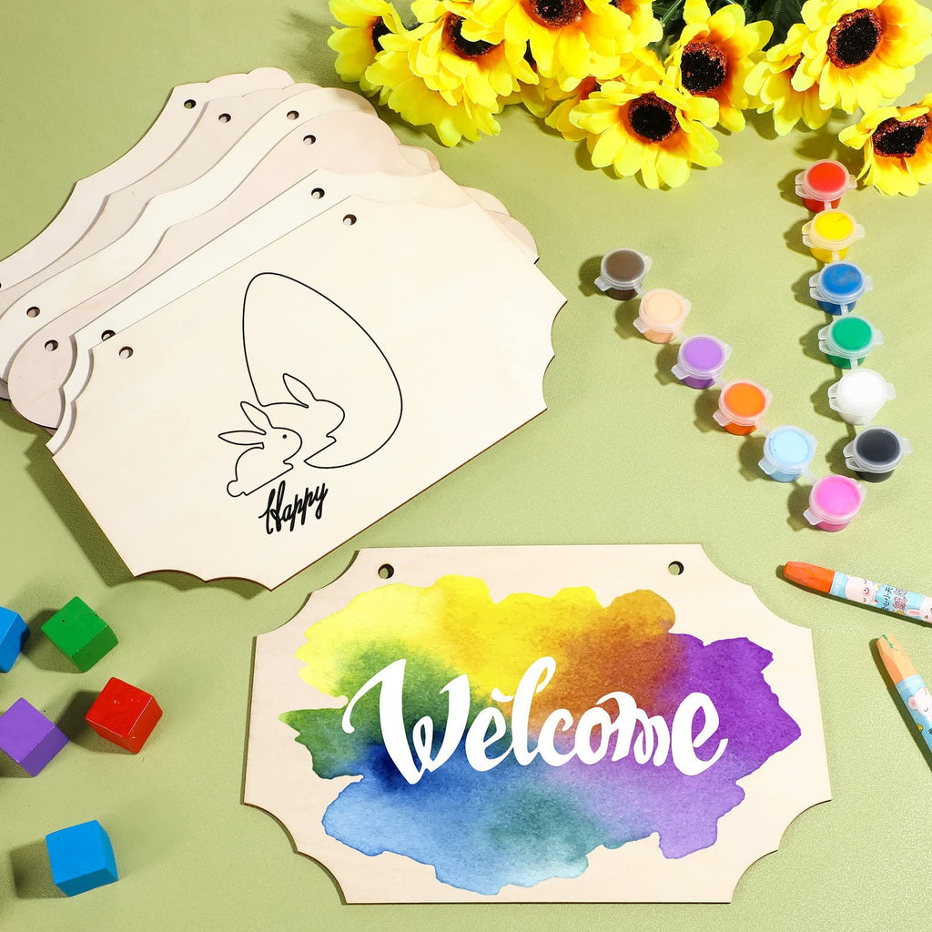 Unfinished wood sign blanks with Easter bunny and egg design, and a 'Welcome' sign with watercolor background, surrounded by paints and craft supplies.