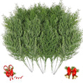 Bundle of artificial green cypress pine branches with red ribbon candy canes and bells on white background