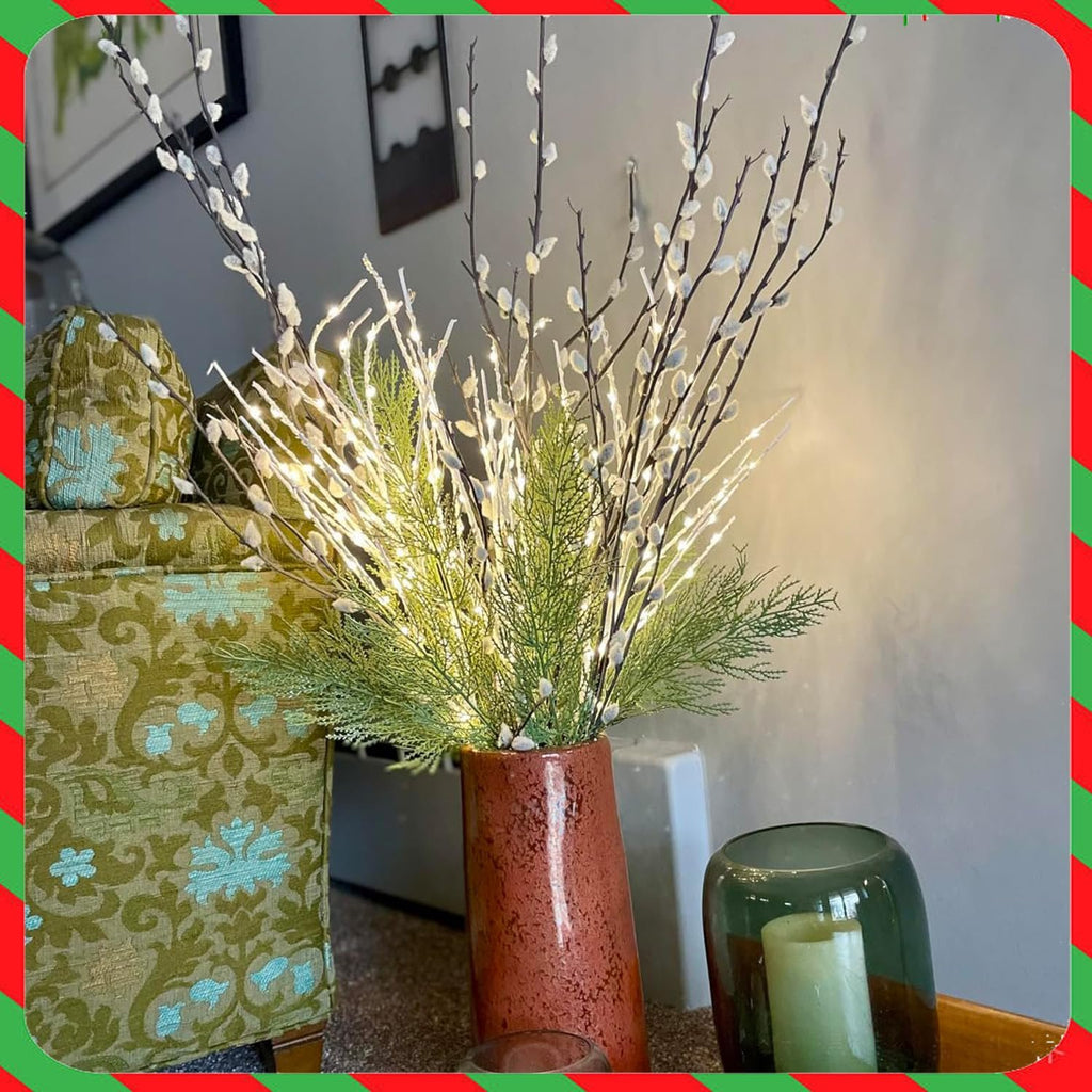 Illuminated artificial cypress pine branches in a vase with a green patterned armchair and candle holder.