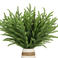 Green faux evergreen sprigs in a white vase with twine detail, close-up view