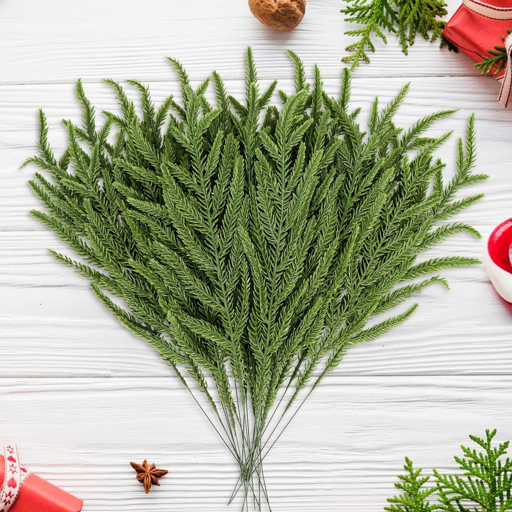 Bundle of 30 green faux Norfolk pine stems arranged on a white wooden surface with Christmas decorations.