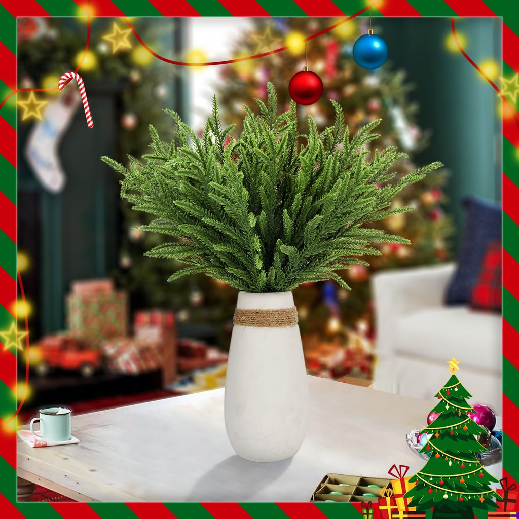 Green faux pine stems in a white vase on a table with Christmas decorations