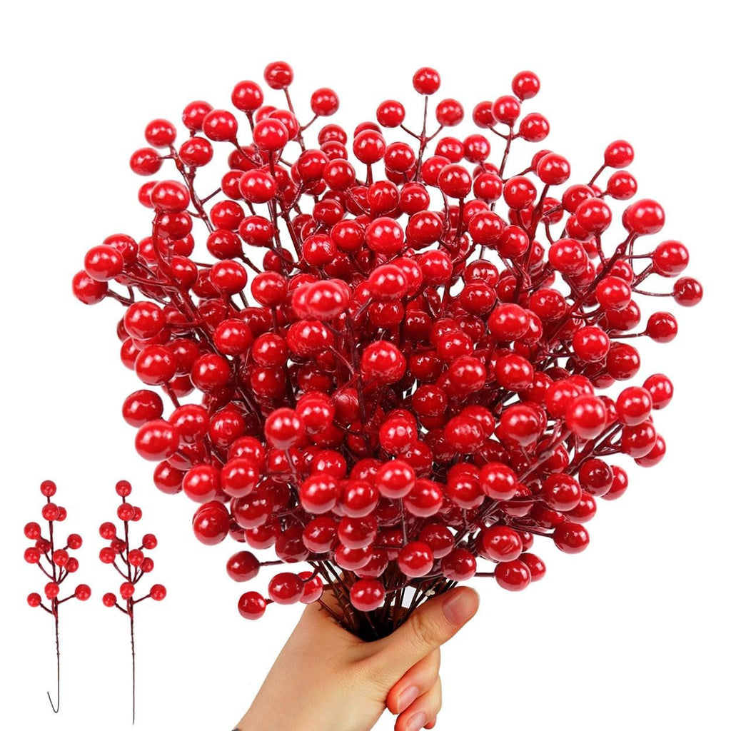 Hand holding a bunch of artificial red berry stems with two smaller stems to the left on a white background.
