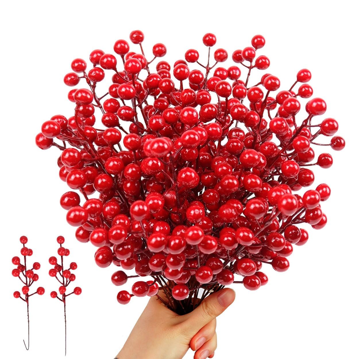 Hand holding a bunch of artificial red berry stems with two smaller stems to the left on a white background.