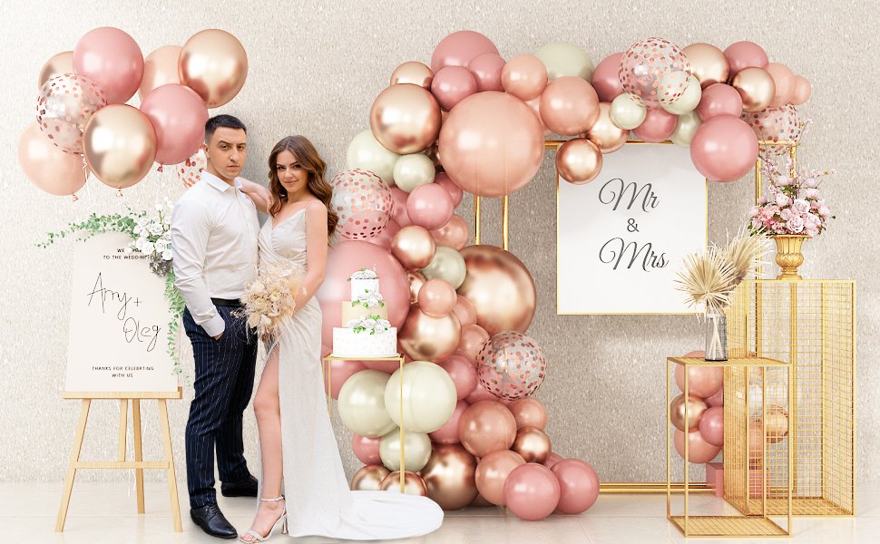 Wedding couple posing by a balloon arch with a cake and signage