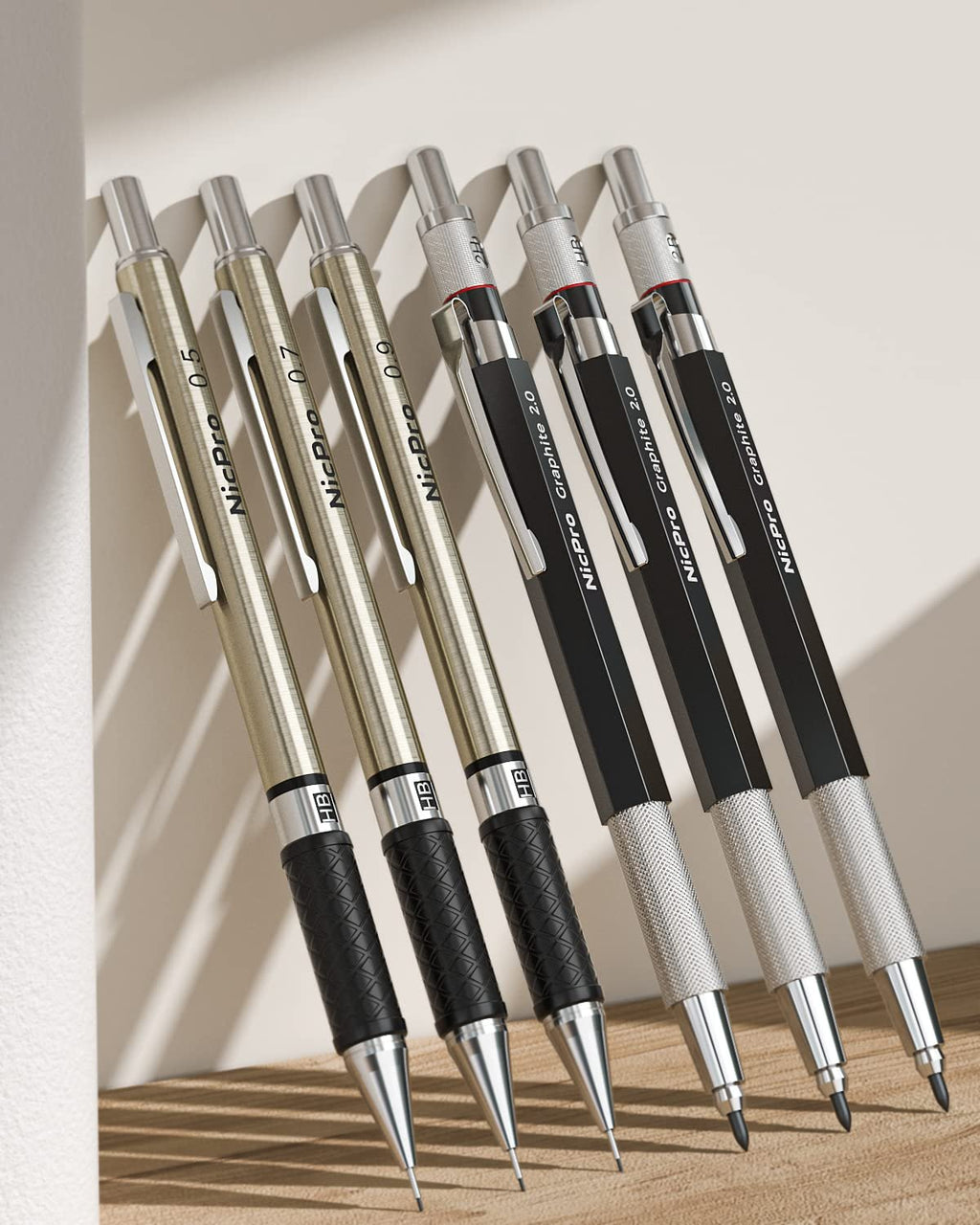 Set of six mechanical pencils in gold and black finishes, angled on a wooden surface with a light wall backdrop.