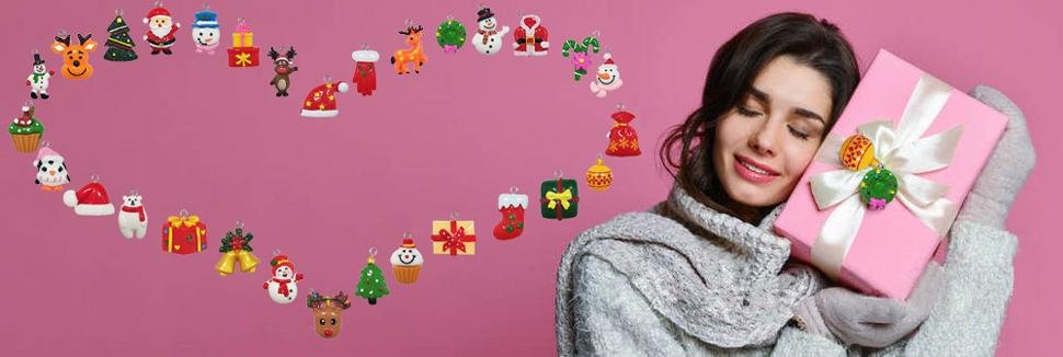 Woman holding a pink gift box with assorted mini Christmas ornaments arranged in a heart shape on a pink background
