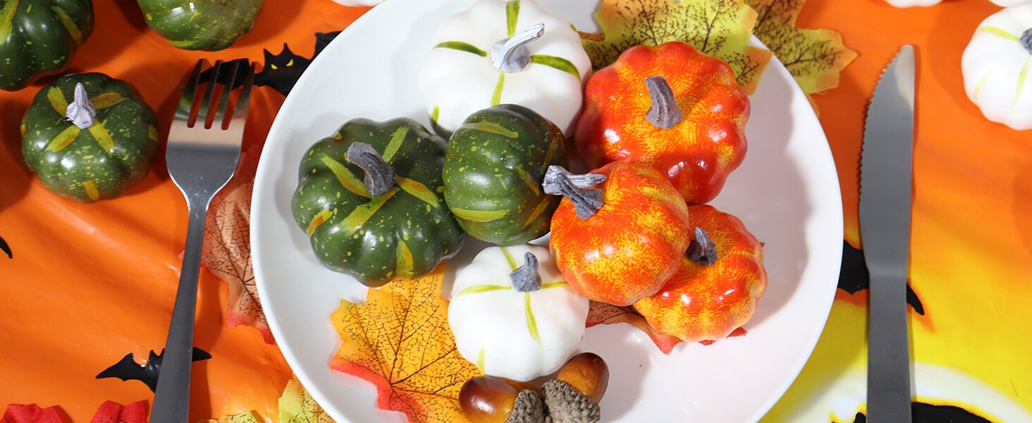Assorted mini pumpkins on a white plate with fall leaves, fork, and knife