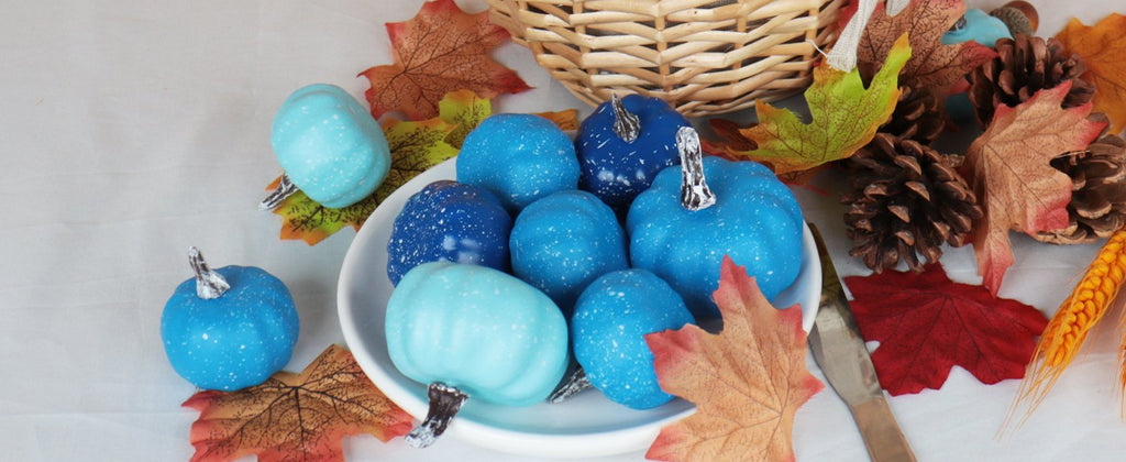 Assorted blue mini pumpkins with white speckles arranged with fall leaves and pinecones in a basket.