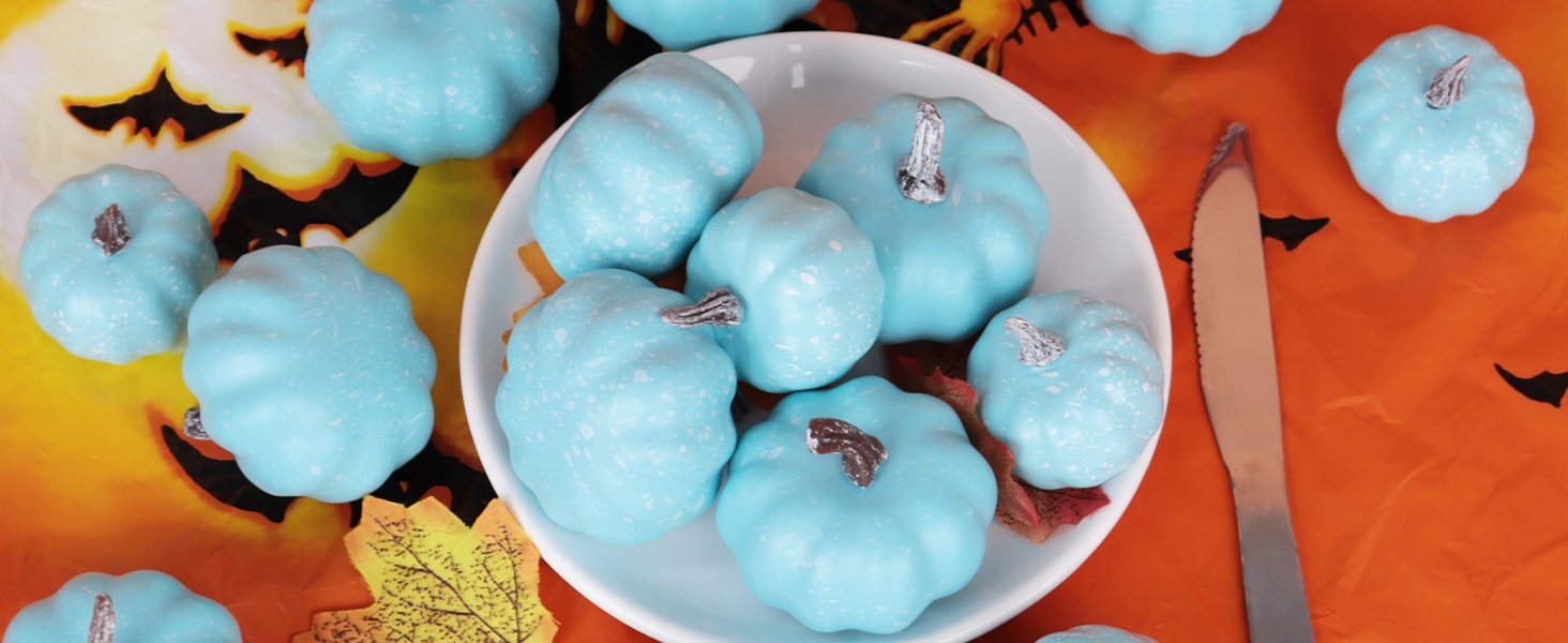 Assorted light blue mini pumpkins with silver stems arranged on a white plate and around it, with a Halloween-themed orange background featuring bats and a jack-o'-lantern face.