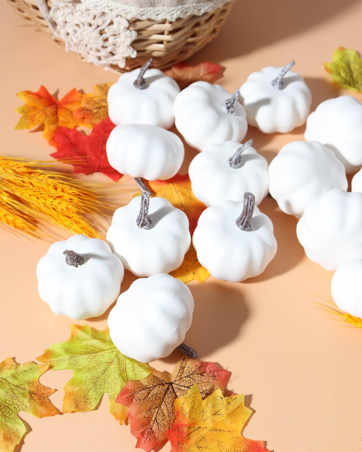 Assorted white mini pumpkins scattered with fall leaves and wheat stalks near a basket.