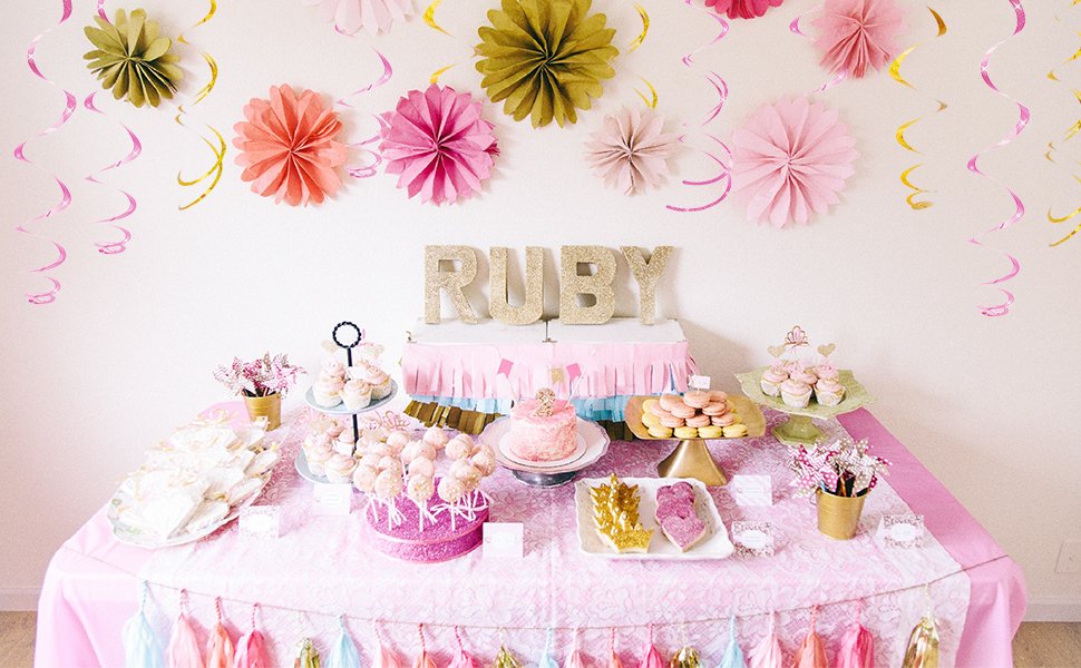 Party table with pink and gold decorations, cake, cupcakes, cookies, and macarons, with the name 'RUBY' spelled out in glitter letters.