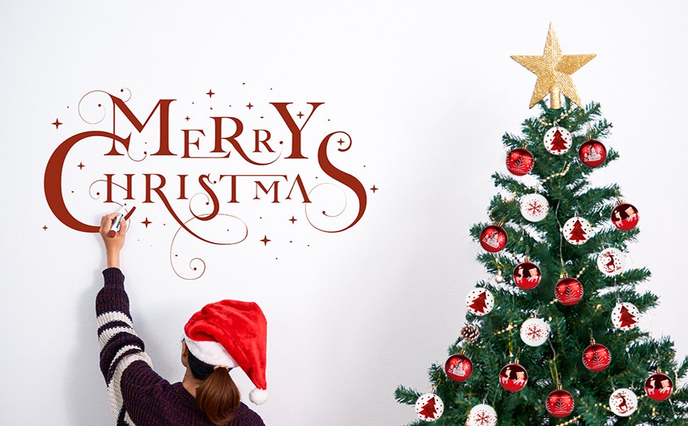 Person in Santa hat writing Merry Christmas on wall next to decorated Christmas tree
