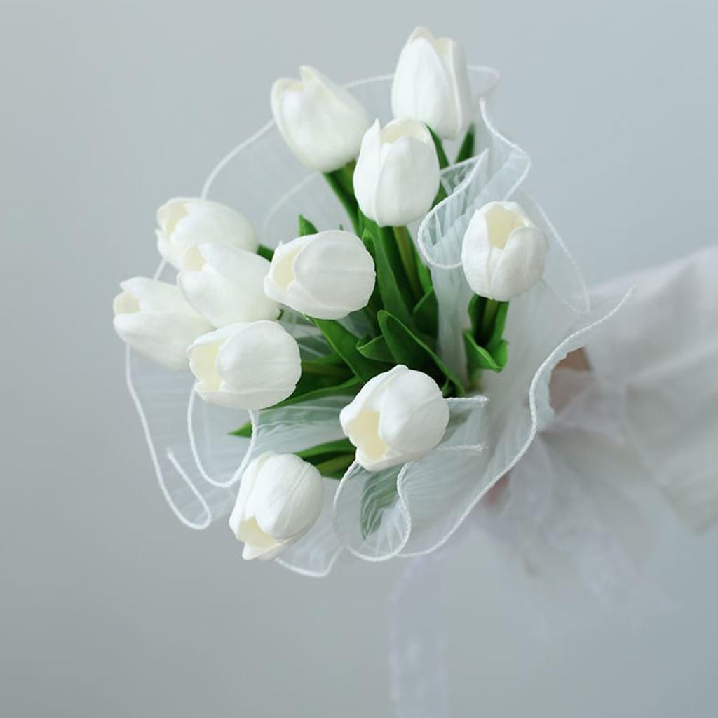 Bouquet of white artificial tulips with green leaves wrapped in sheer white ribbon