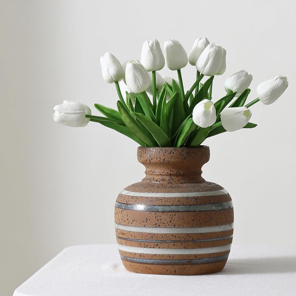 White artificial tulips in a striped ceramic vase on a white tablecloth