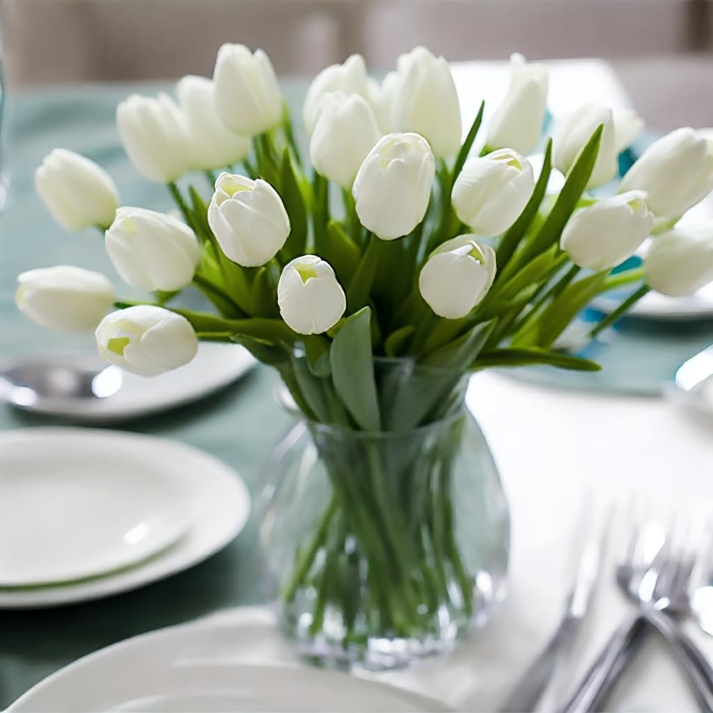 A vase of white artificial tulips arranged on a table setting with plates and silverware.