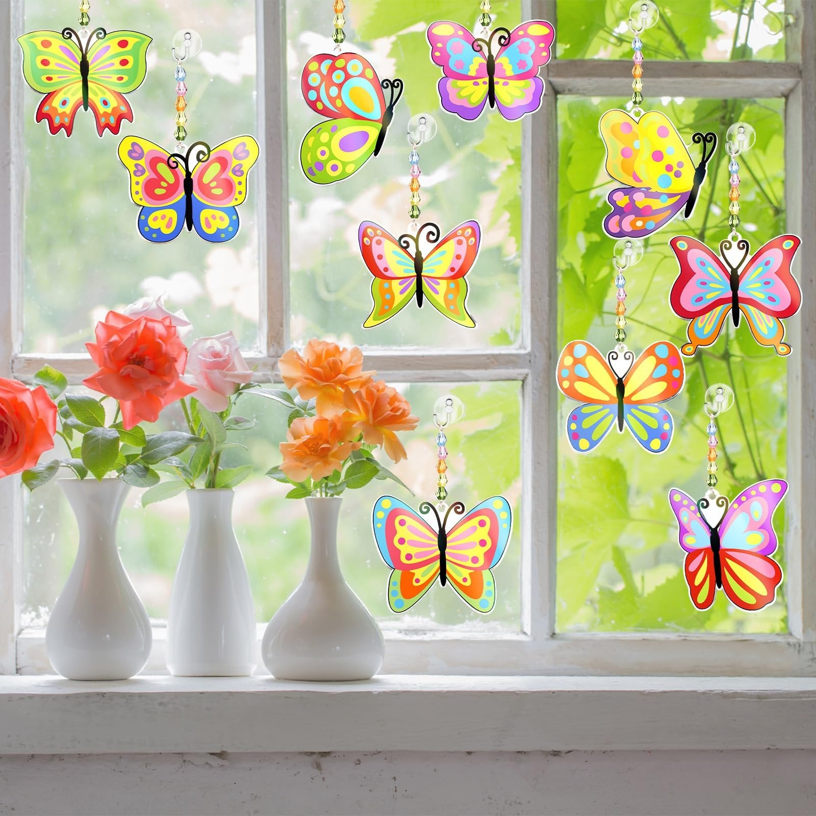 Colorful butterfly suncatchers hanging in a window with vases of roses on the sill below