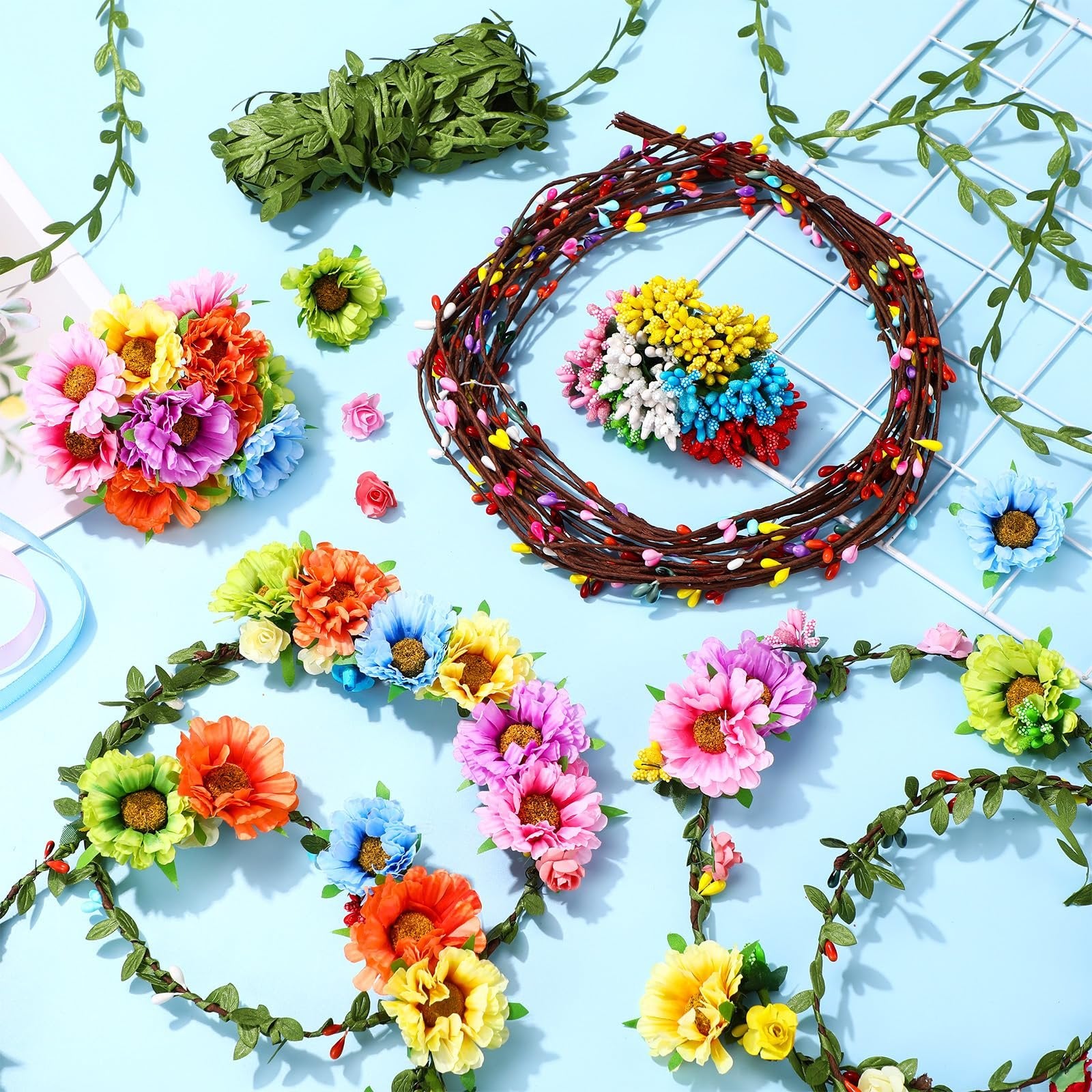 Flower crown making kit components including colorful artificial flowers, green leaf vines, and rattan bases arranged on a light blue background.