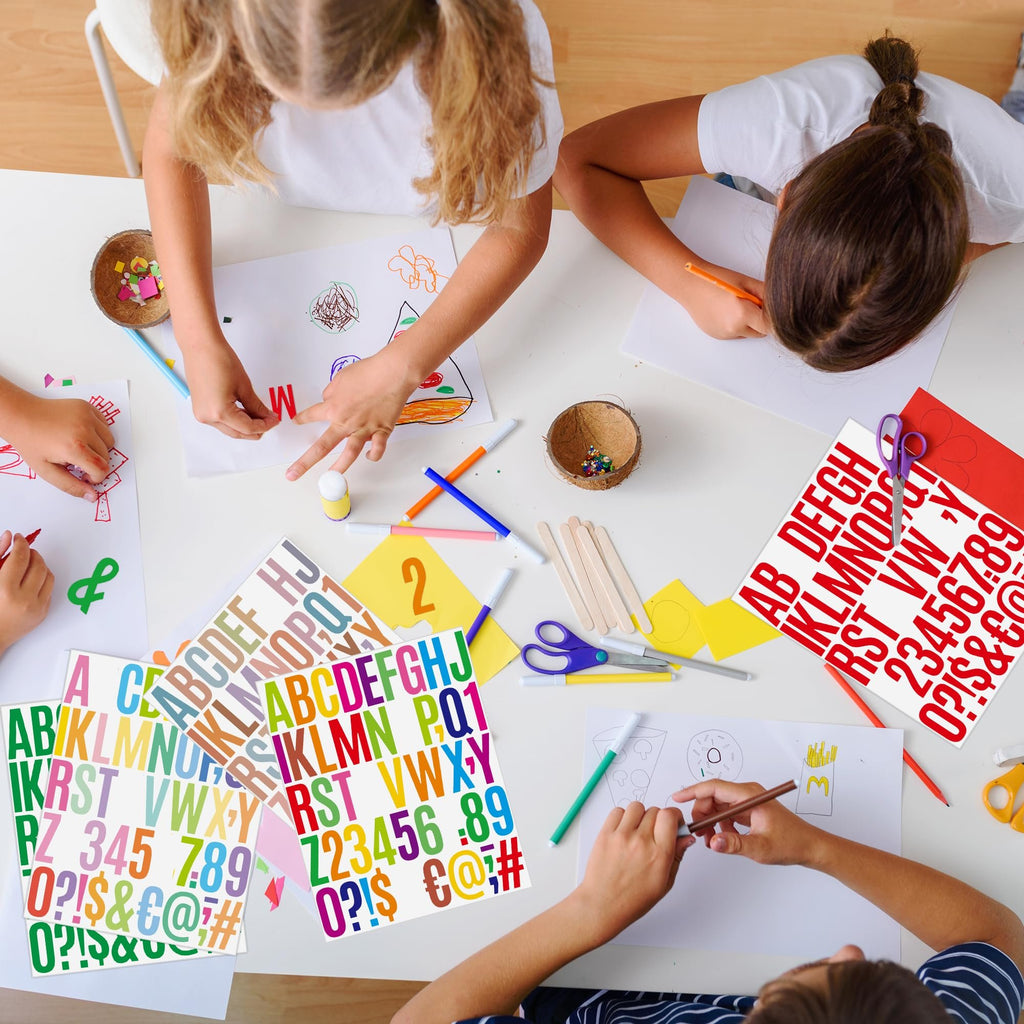 Children crafting at a table, using colorful alphabet and number stickers for art projects. Overhead view.