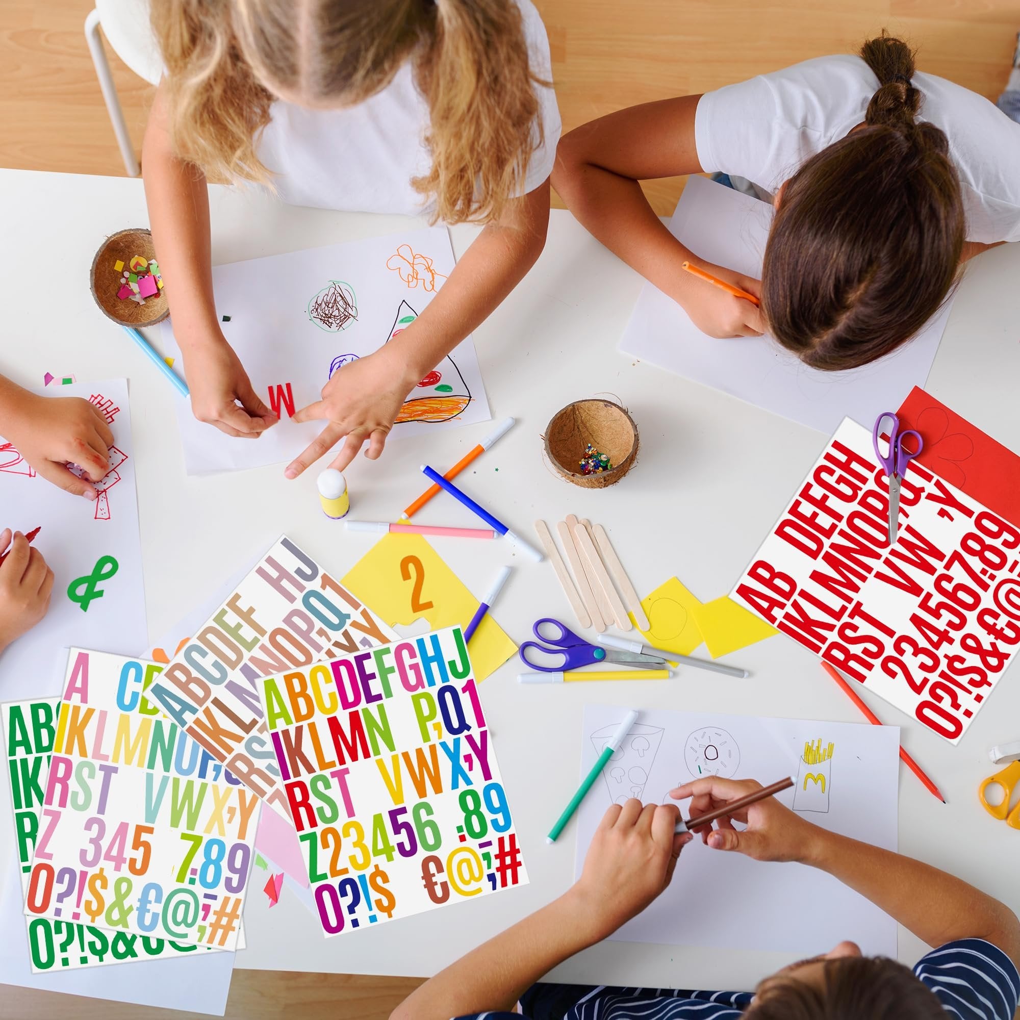 Children crafting at a table, using colorful alphabet and number stickers for art projects. Overhead view.