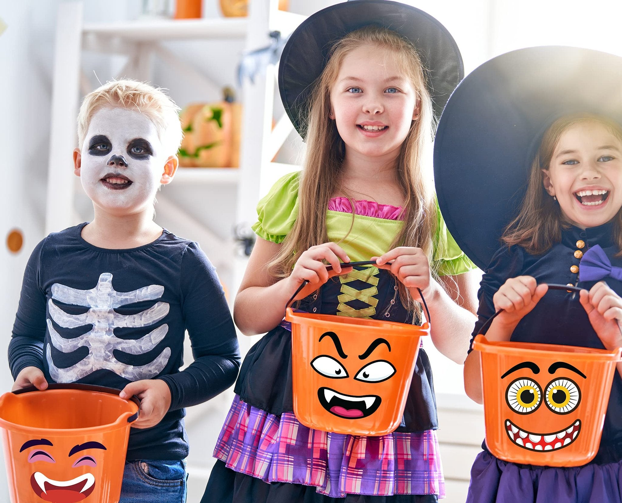 Three children in Halloween costumes holding trick-or-treat buckets with cartoon faces