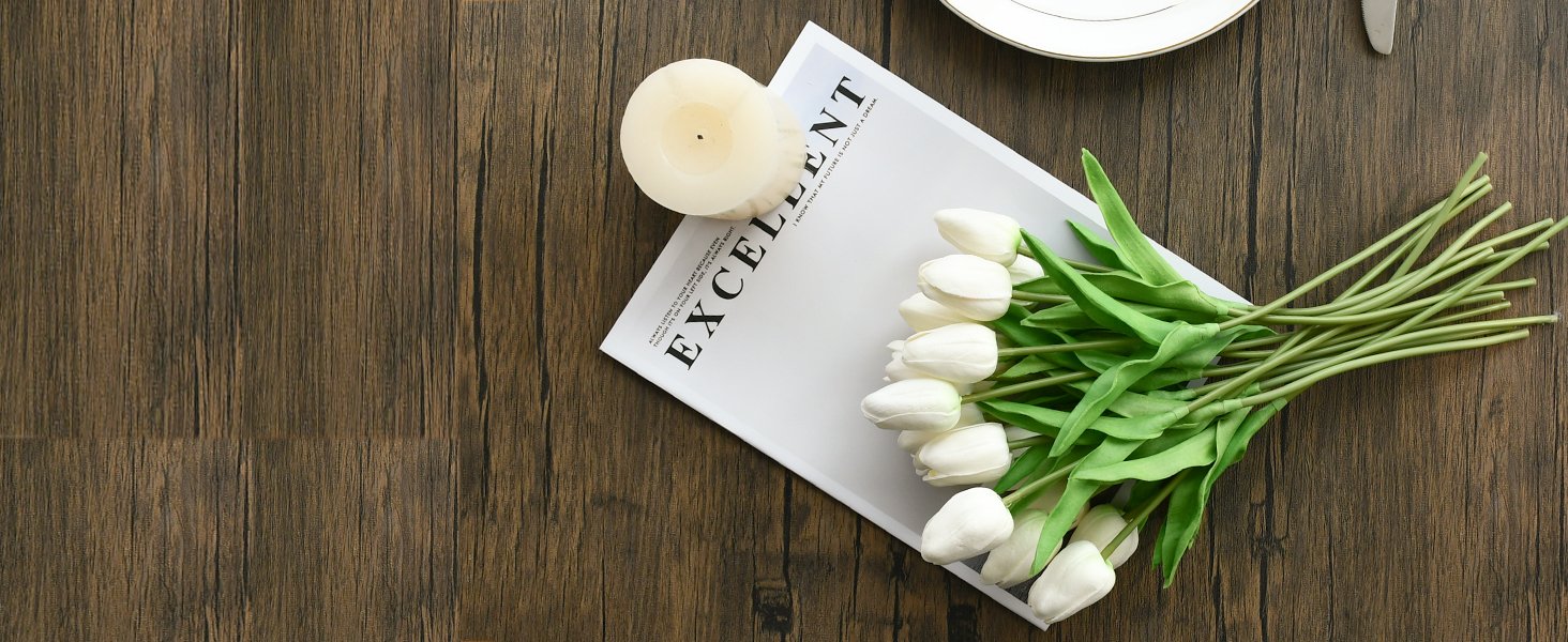 White artificial tulips and a candle on a magazine with the word EXCELLENT, set on a wooden table.