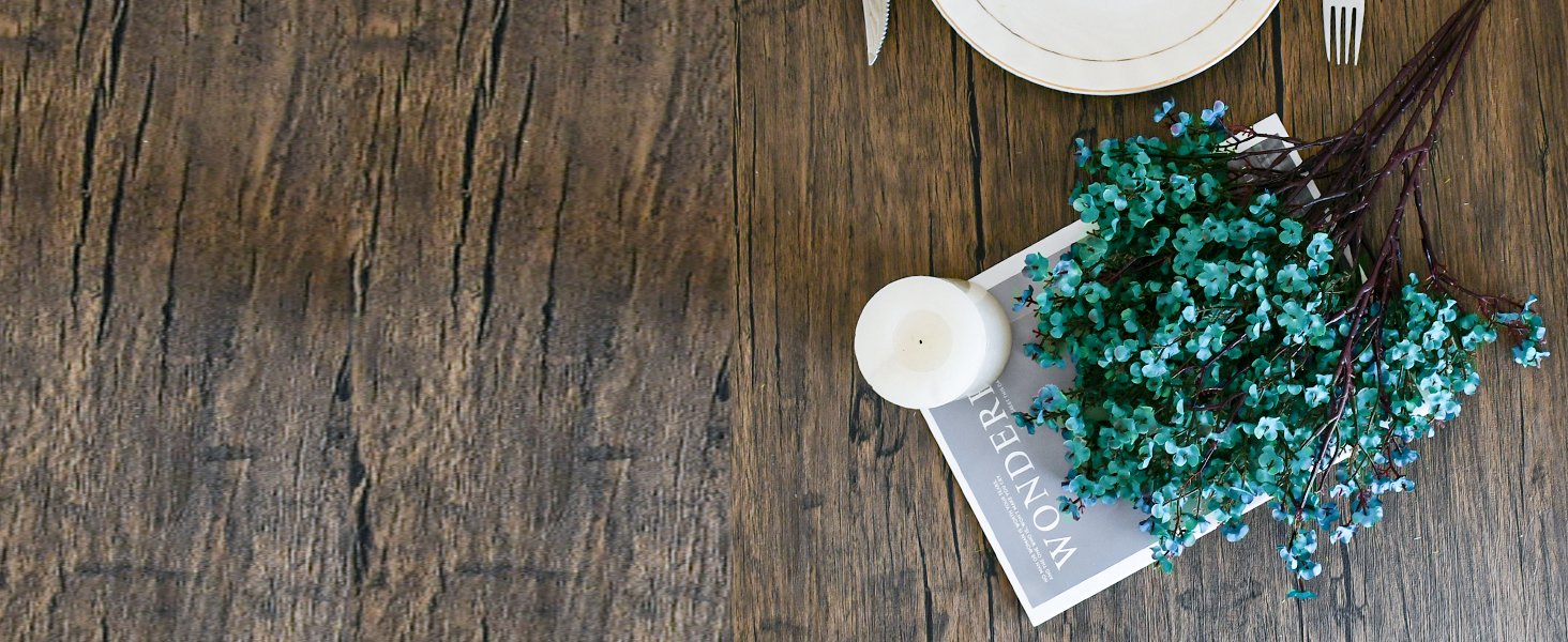 Artificial blue flowers and a white candle on a magazine with the word WONDER visible, set on a wooden table with a plate and cutlery.