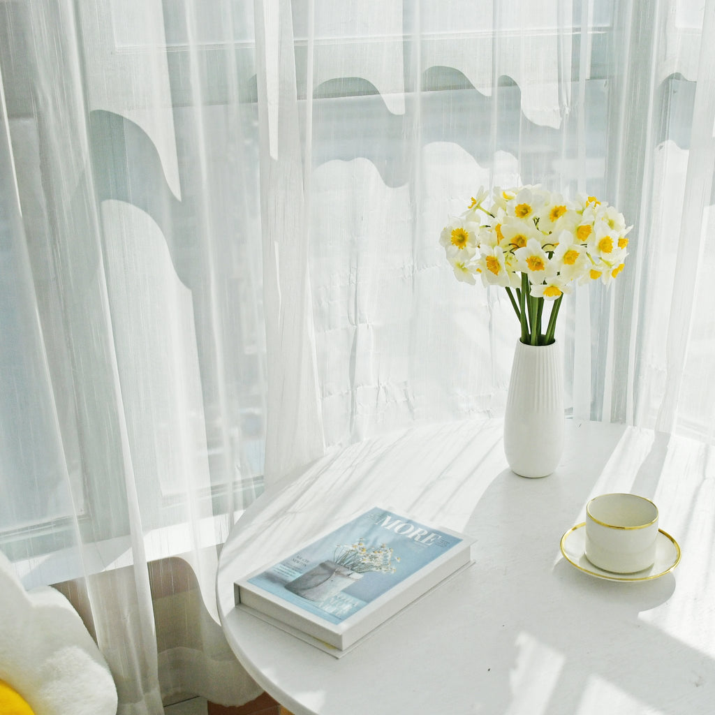 Bouquet of white and yellow daffodils in a white vase on a table with a book and teacup