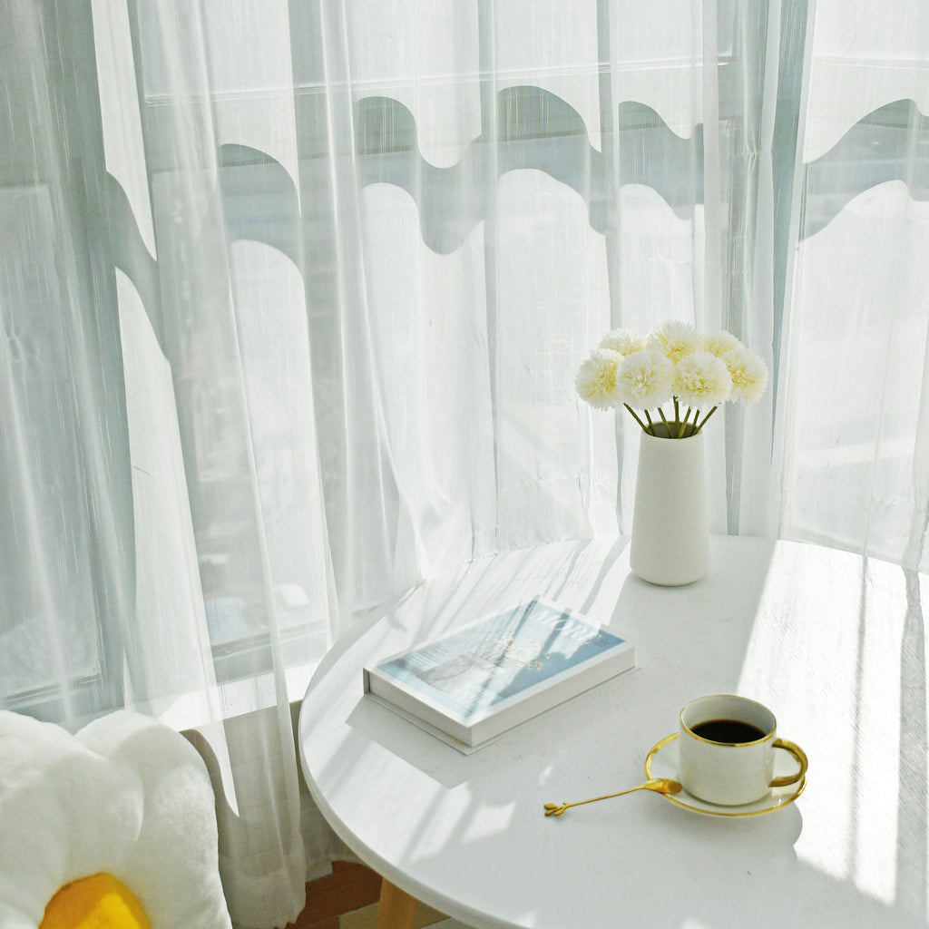 White vase with cream artificial flowers on a round table next to a book and coffee cup