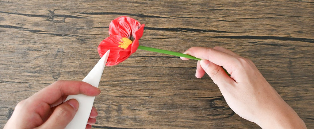 Hands assembling a red artificial poppy flower on a wooden surface