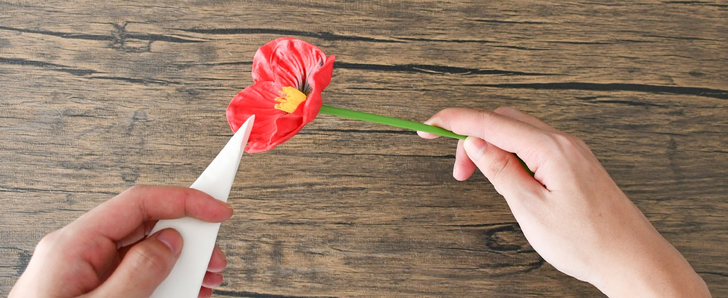 Hands assembling a red artificial poppy flower on a wooden surface
