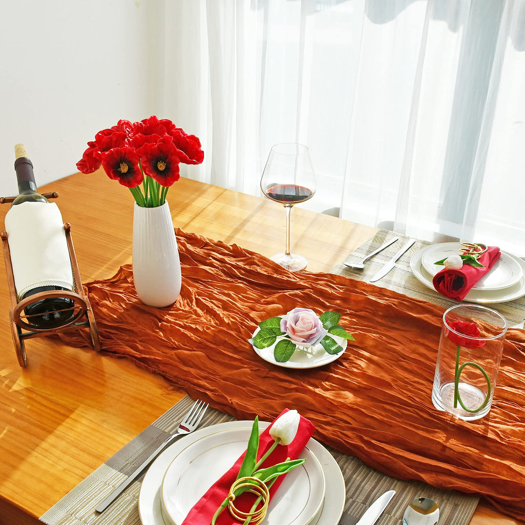 Table setting with red artificial poppies in a vase, wine bottle, and place settings with red napkins and artificial flowers.