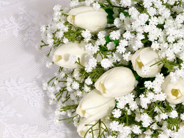 Close-up of white artificial tulips and baby's breath flowers on a white lace background