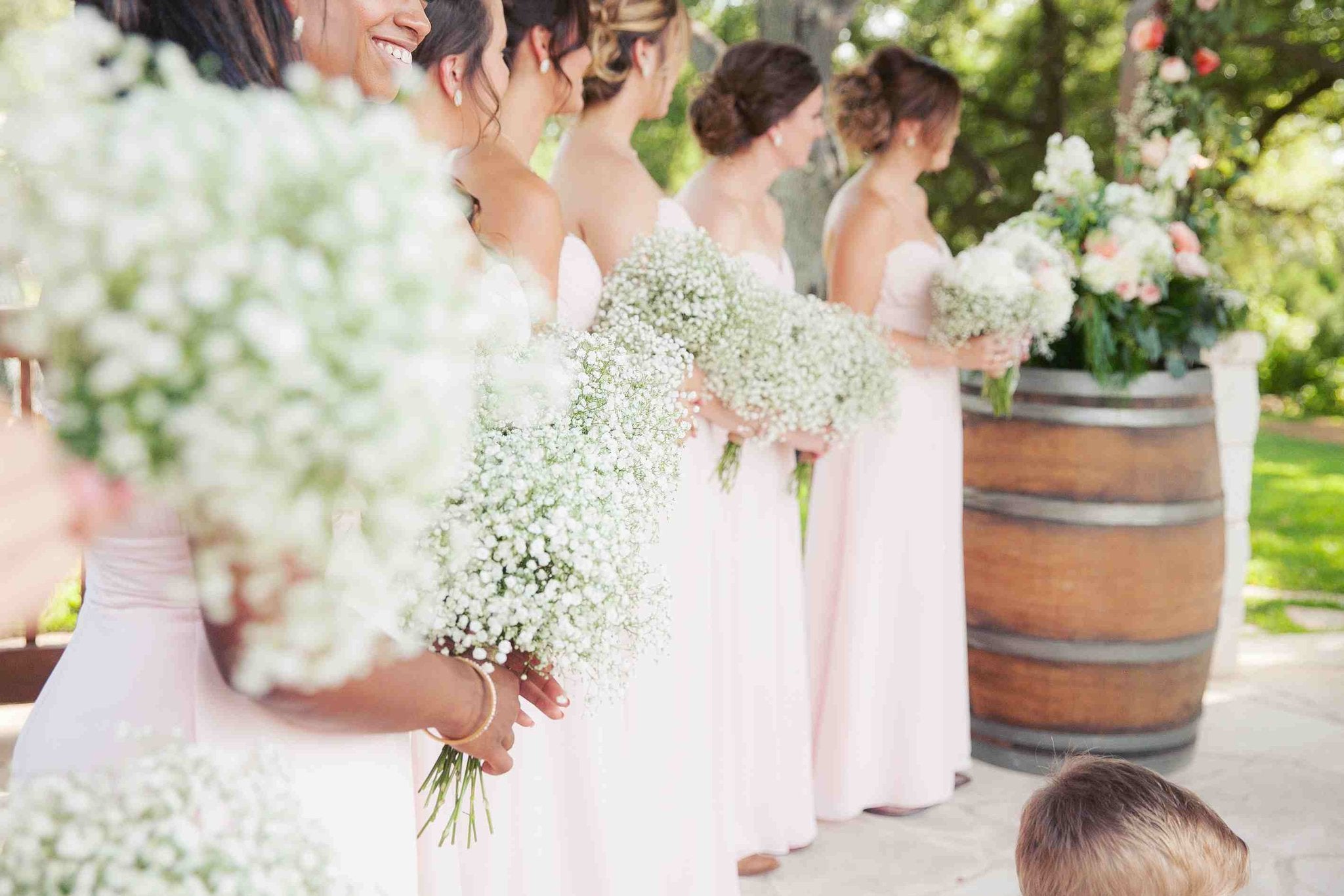 Bridesmaids in light pink dresses holding bouquets of white baby's breath flowers at an outdoor wedding ceremony.