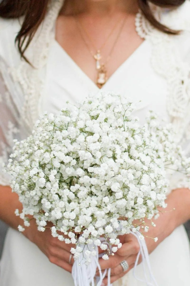 Bride holding a bouquet of artificial baby's breath flowers with white lace shawl and necklaces