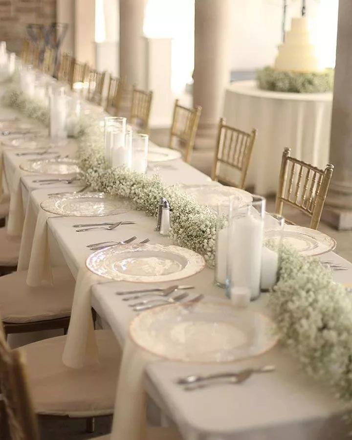 Long banquet table set for a wedding reception with white baby's breath floral runner and candles