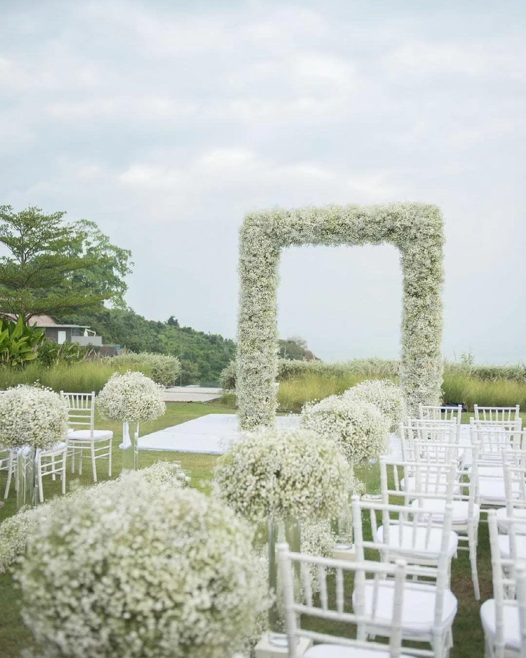 Outdoor wedding ceremony setup with a square arch and rows of white chairs decorated with baby's breath flowers.