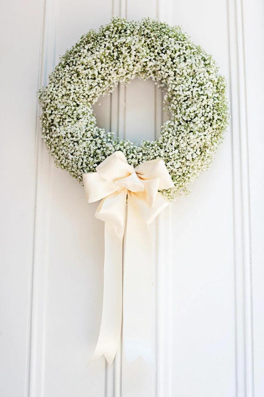 Artificial baby's breath wreath with a cream ribbon bow hanging on a white paneled door